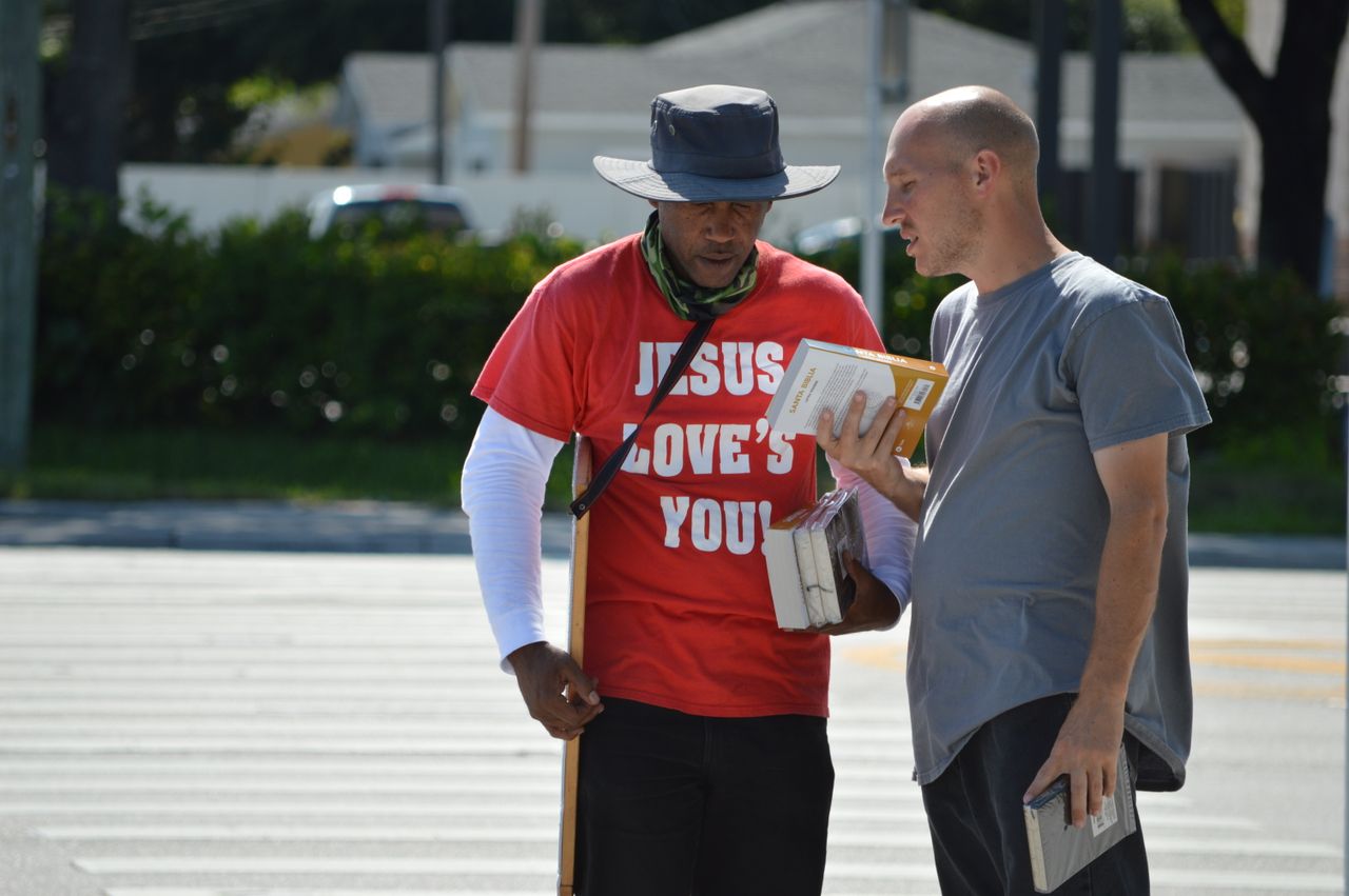 Services Two men engage in a religious conversation on a city street, holding books.