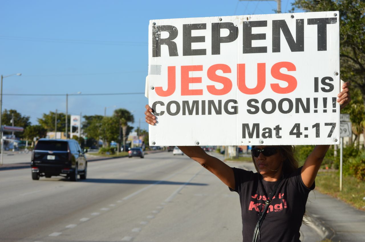 Services Woman holding a religious billboard on a street, emphasizing faith and repentance.