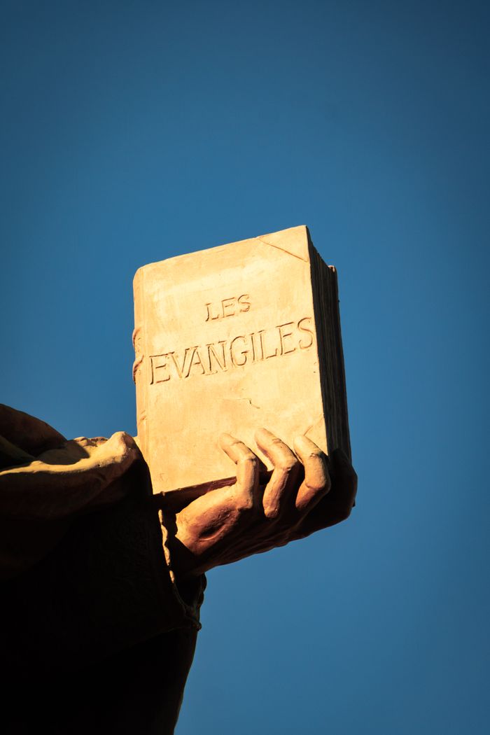 Crafting Captivating Headlines: Your awesome post title goes here A statue hand holds "Les Evangiles" book against a clear blue sky, symbolizing spirituality.